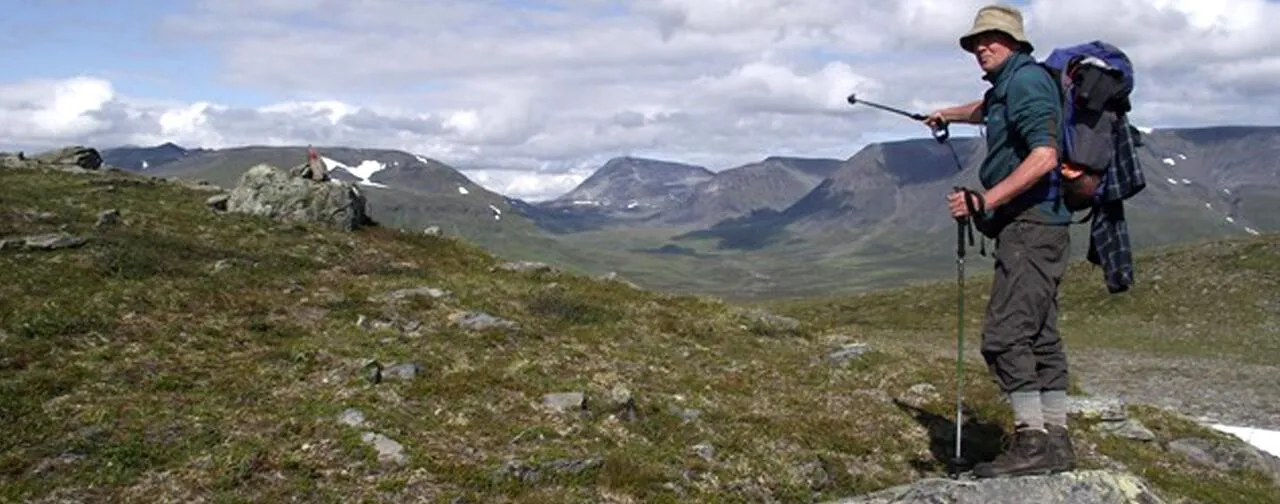 Alan Wilkinson with walking poles and rucksack, pointing across a valley inside the Arctic Circle